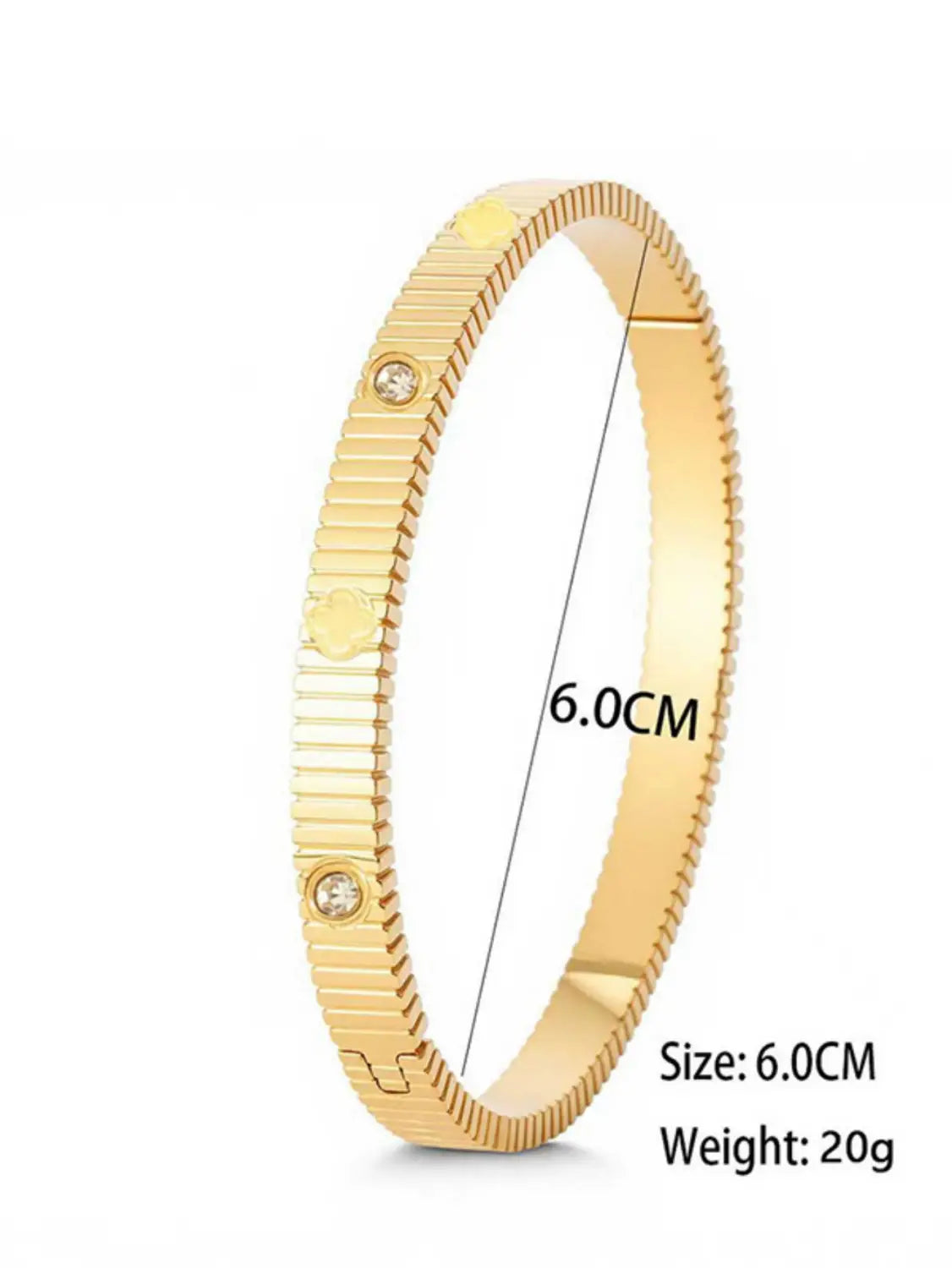Pulsera tipo brazalete con cruz de cristal con acabado dorado, con exterior acanalado y texturizado y tres piedras preciosas transparentes incrustadas.