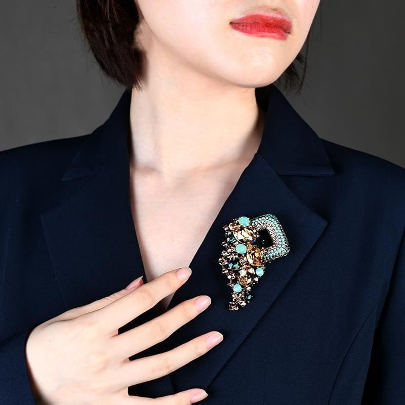 A crystal flower brooch pin for women featuring sparkling turquoise and gold-toned crystals pinned to a navy blazer.