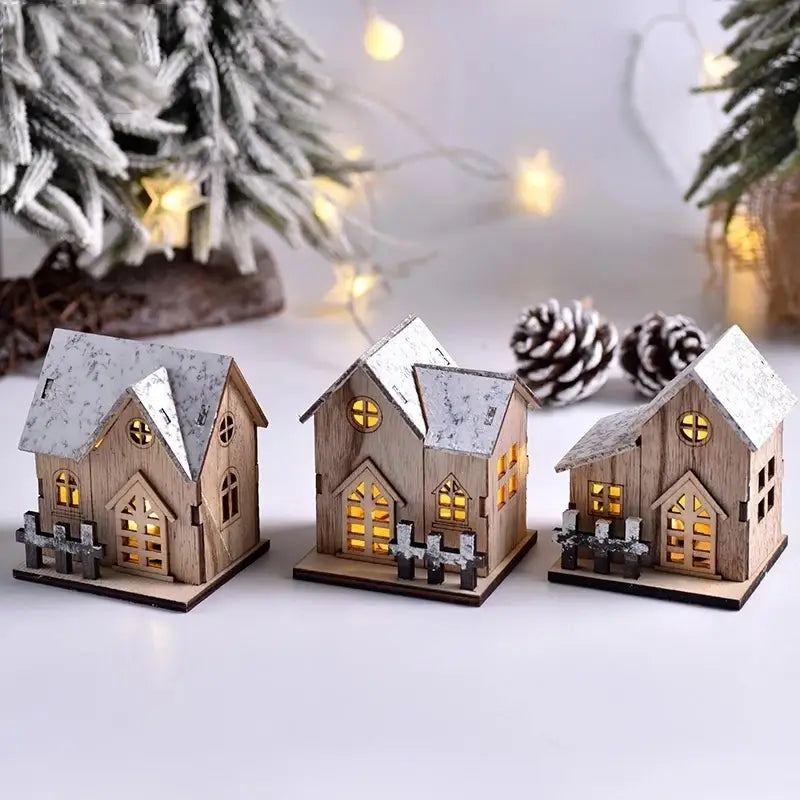 Drei Miniatur-Holz-Weihnachtshäuser mit schneebestäubten Dächern und leuchtenden gelben LED-Lichtern als leuchtende Weihnachtsdekorationen.