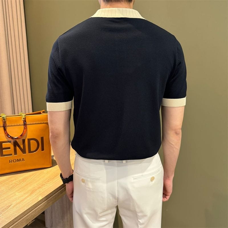Camiseta tipo polo de punto azul marino de manga corta con cuello acanalado color crema y puños de las mangas, que muestra un diseño con bloques de color.