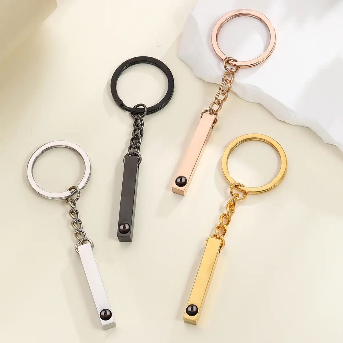 four sleek rectangular metal custom photo projection keychains in silver black rose gold and yellow gold finishes with matching chains and small dark spherical accents personalized memorial gift