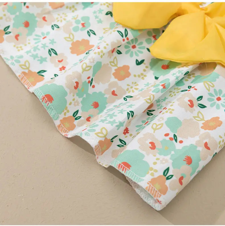 A soft white fabric floral dog princess dress with pastel mint green peach and coral patterns and a bright yellow bow at the waist.