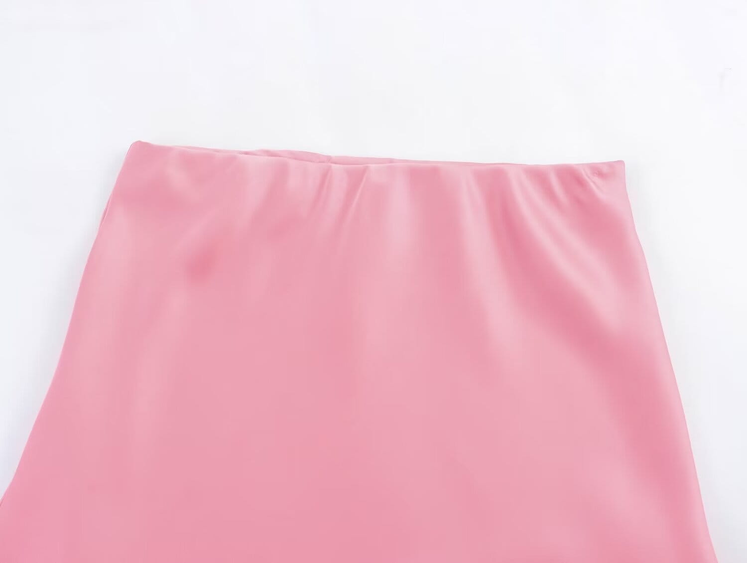 Une jupe midi en satin rose tendre, à taille haute et plis délicats le long du tissu lisse et fluide.