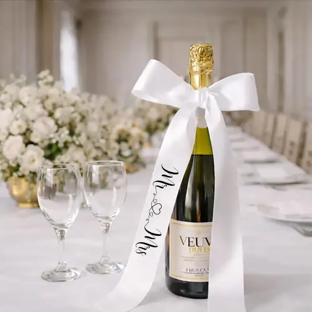 ヴーヴ・クリコのシャンパンボトルに、白いサテンの「Just Married（新婚）」用ワインボトルリボンの蝶結びをあしらい、結婚式の装飾として、エレガントな黒い筆記体で「Mr and Mrs」と記された文字を特徴としています。