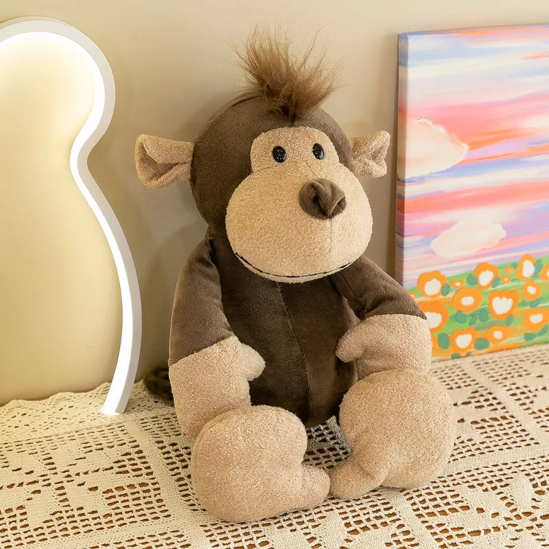 Un peluche de animal de la jungla que presenta un mono de tela marrón y beige suave, con un mechón de pelo en la cabeza, rasgos faciales cosidos y ojos negros tipo botón.