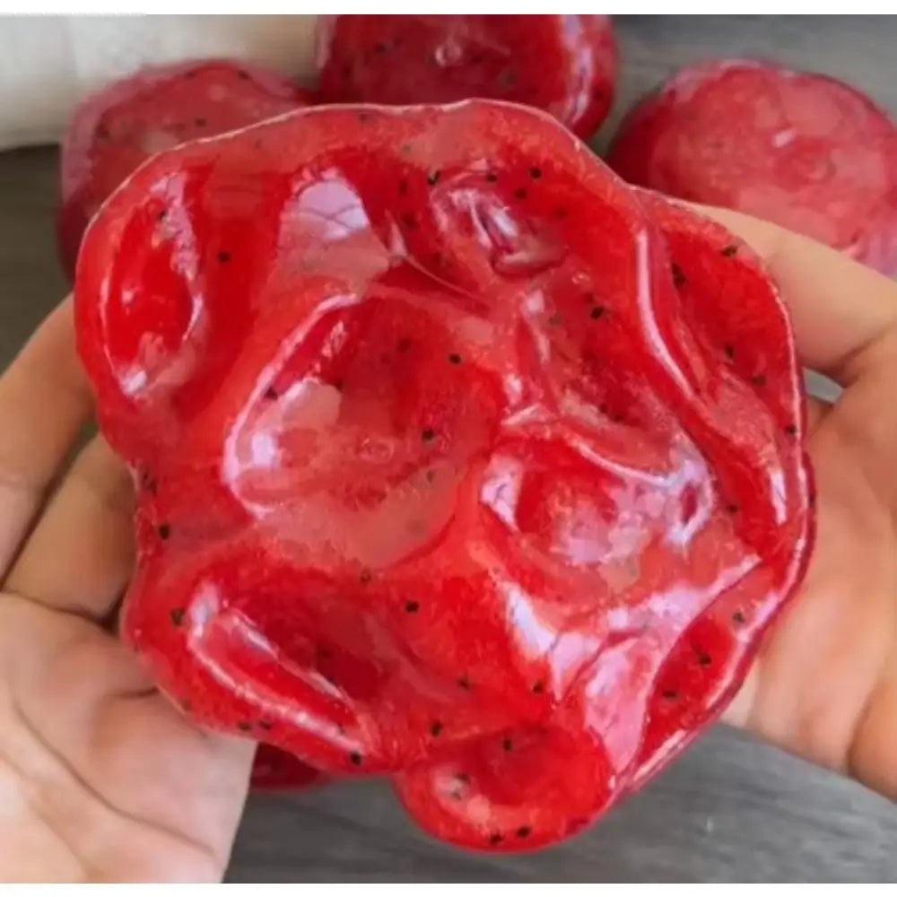un juguete artesanal de granizado de sandía con rebote lento para aliviar el estrés, con forma de jabón de fruta del dragón rojo vibrante y brillante, con textura translúcida y semillas negras incrustadas en todo el interior