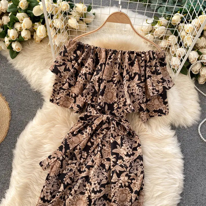 Enterizo de pierna ancha negro y beige con estampado floral y escote tipo bardot, con mangas con volante, exhibido en una percha de madera