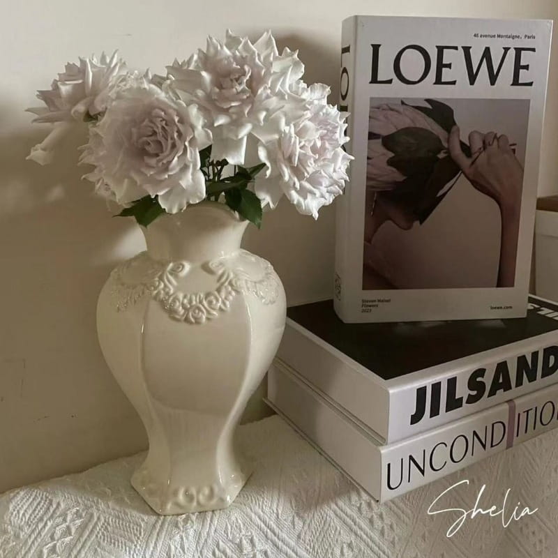 Un jarrón de cerámica moderno francés blanco con intrincados detalles de relieve floral que sostiene un ramo de delicadas rosas de color claro para una decoración elegante del hogar.