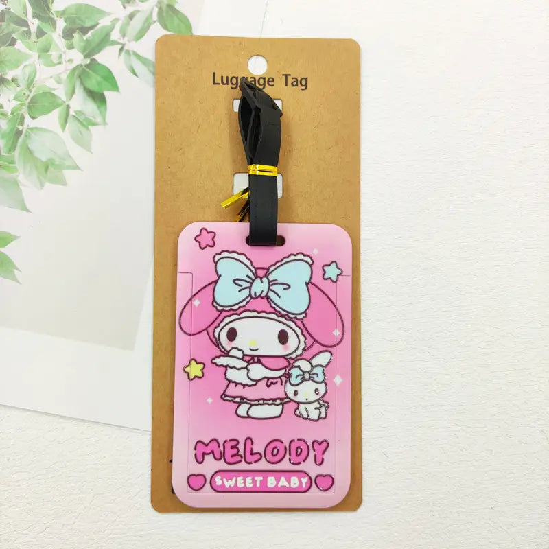 Étiquette de bagage Hello Kitty en silicone rose comportant le personnage Melody, avec un nœud bleu clair et des accents en forme d’étoiles, fixée à une sangle noire pour l’identification de la valise.