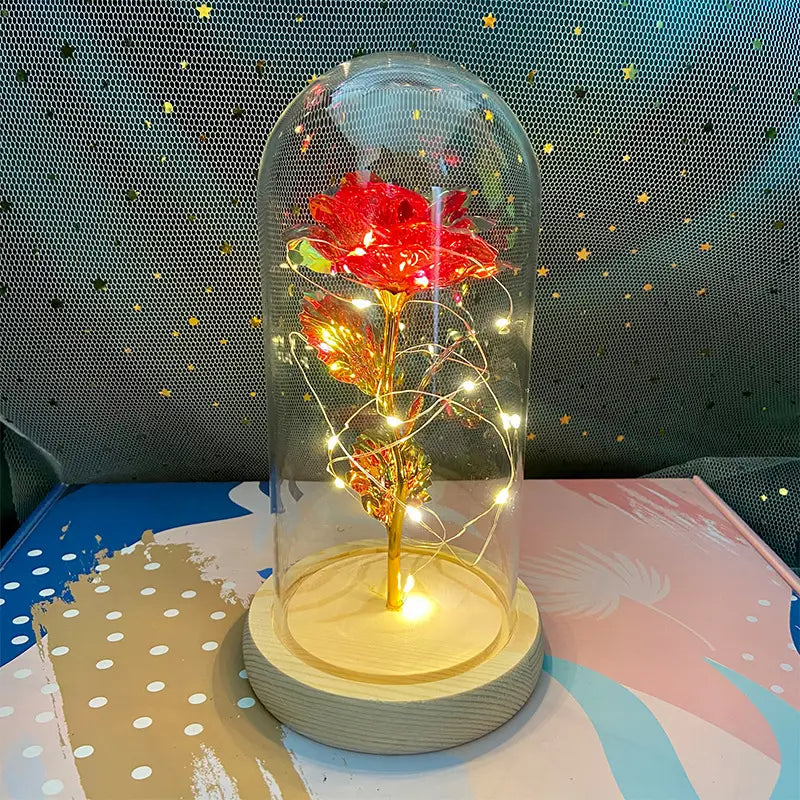 Eine leuchtend rote und goldene „Eternal Gold Rose“, umschlossen in einer klaren Glaskuppel mit eingebetteten LED-Feenlichtern, Geschenk