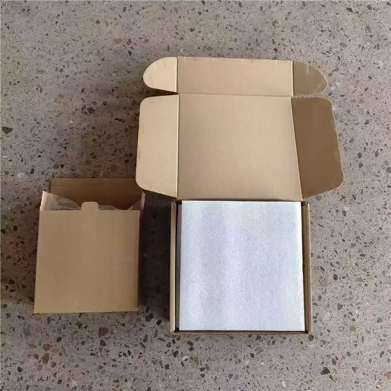 a white square-shaped wooden gymnastics ring wrapped in protective foam inside an open cardboard box with numbered straps visible