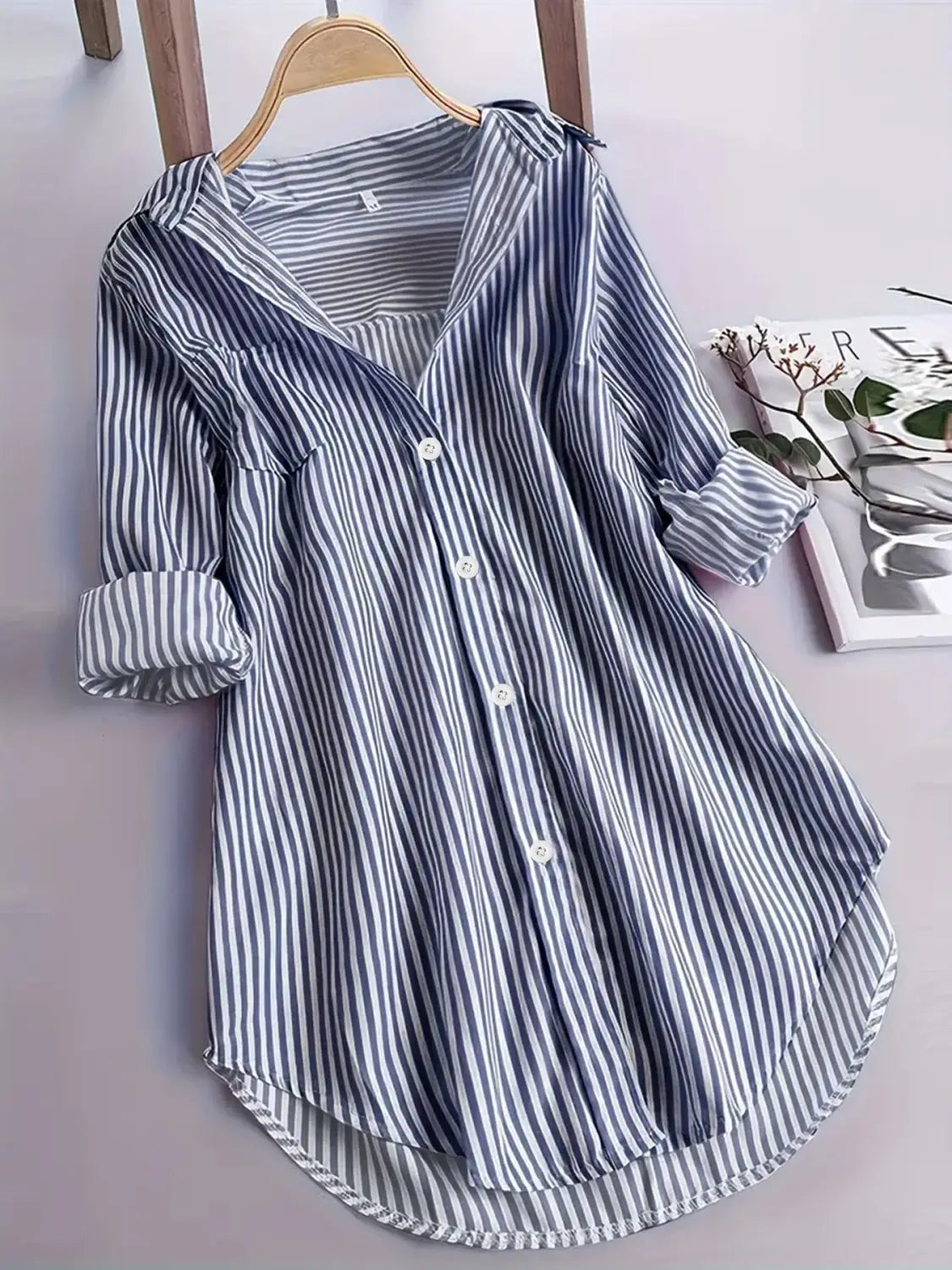 Chemise boutonnée décontractée à rayures verticales bleu marine et blanches à manches longues, manches retroussées, suspendue à un cintre en bois.