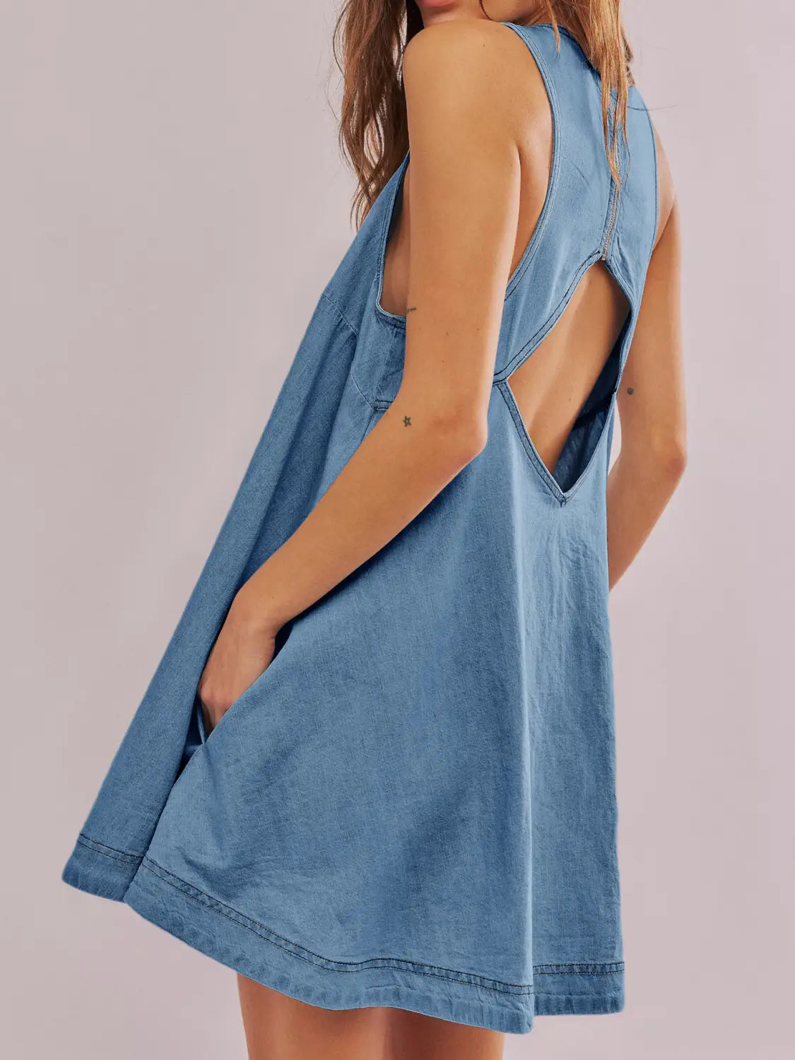 Ein hellblaues Jeans-Minikleid, von der Rückseite gezeigt, mit einem hinten offenen Schleifen-Detail und einem Ausschnitt-Design