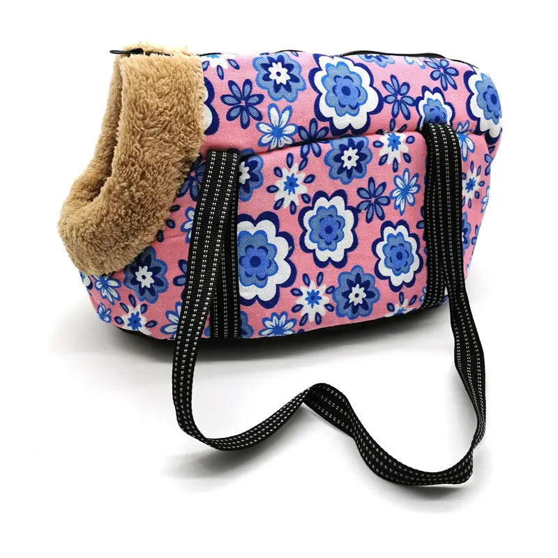 Pink floral-patterned warm pet carrier canvas fleece travel bag with blue and white flowers, tan fleece-lined opening, and black webbing straps.