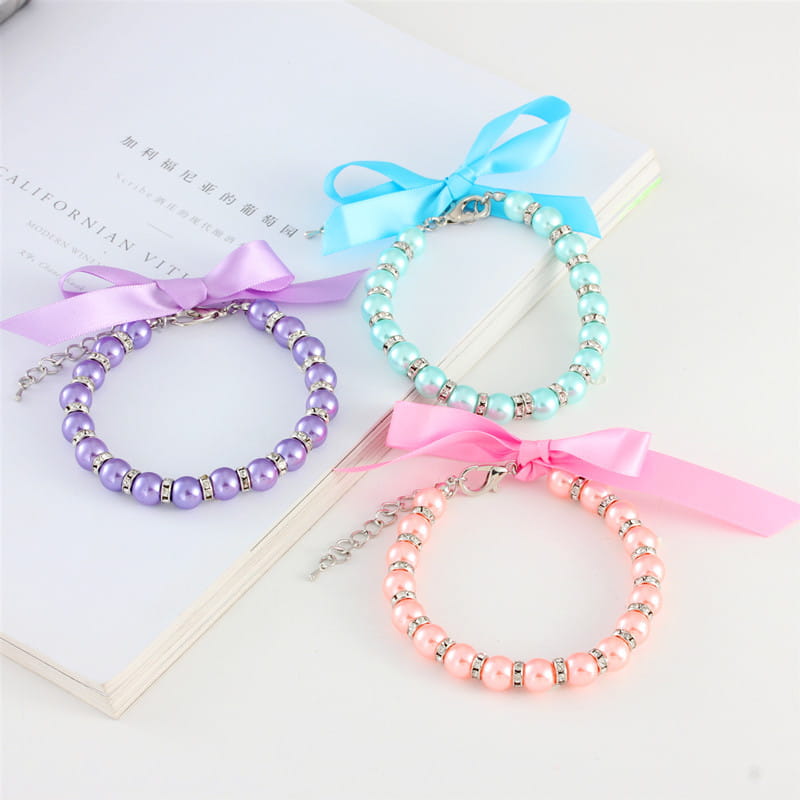trois colliers de perles pour animal à ruban pastel de couleurs assorties, chacun orné d’accents de strass argentés et d’un nœud en satin assorti.