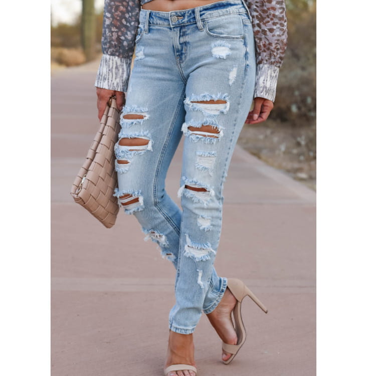 Los pantalones vaqueros ajustados tipo skinny de mezclilla con efecto lavado claro desgastados con roturas presentan múltiples cortes desgastados y bordes deshilachados en un tejido vaquero de primera calidad.