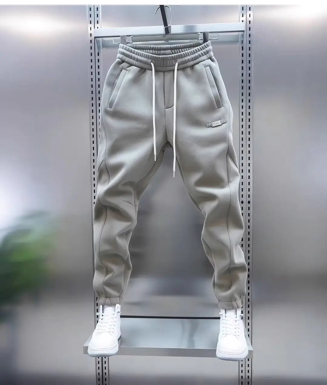 Mens casual solid color sweatpants in gray with white drawstrings and a small logo on the thigh hanging on a metal rack.