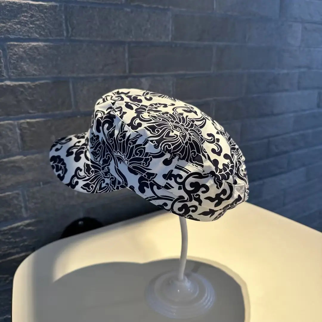 Gorra tipo bucket hat floral elegante con patrón damasco negro y blanco, estilo coreano, impresa, mostrada sobre un soporte de plástico transparente.
