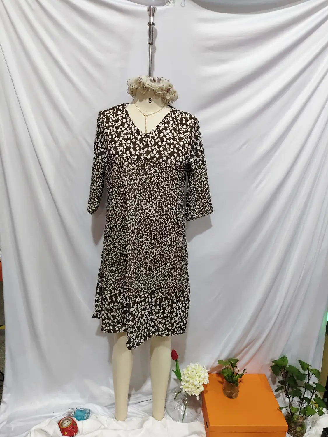 Une robe midi à imprimé floral marron et blanc, encolure en V et manches trois-quarts, présentée sur un mannequin.