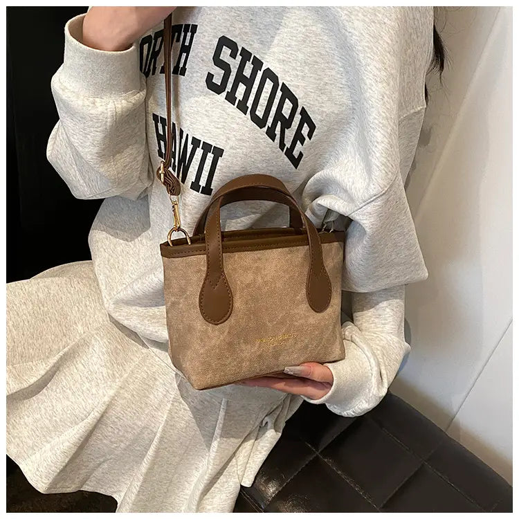 A beige suede retro bucket bag mini tote with brown leather handles and trim designed as a textured canvas shoulder handbag.
