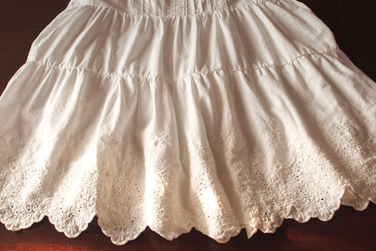 Ein weißes Spitzenkleid mit Volants (gestufter Rock), das einen zarten bestickten Rock mit ausgestellter, gestufter Silhouette und aufwendigen Spitzen-Details entlang des Saums aufweist.