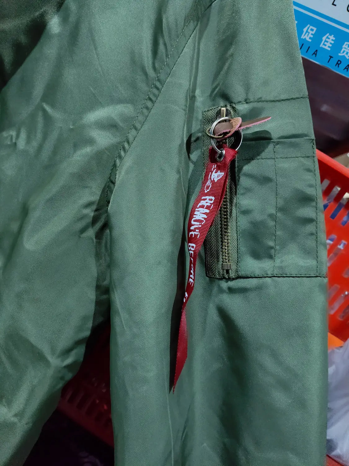 A green ma1 pilot bomber jacket with casual stand collar features a red lanyard with white text hanging from the zipper pull.