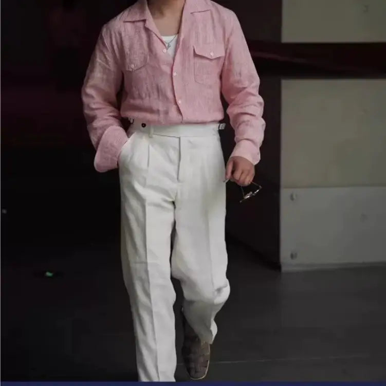 A soft pink long sleeved button up shirt with a subtle textured weave and two chest pockets paired with high waisted linen trousers for men.