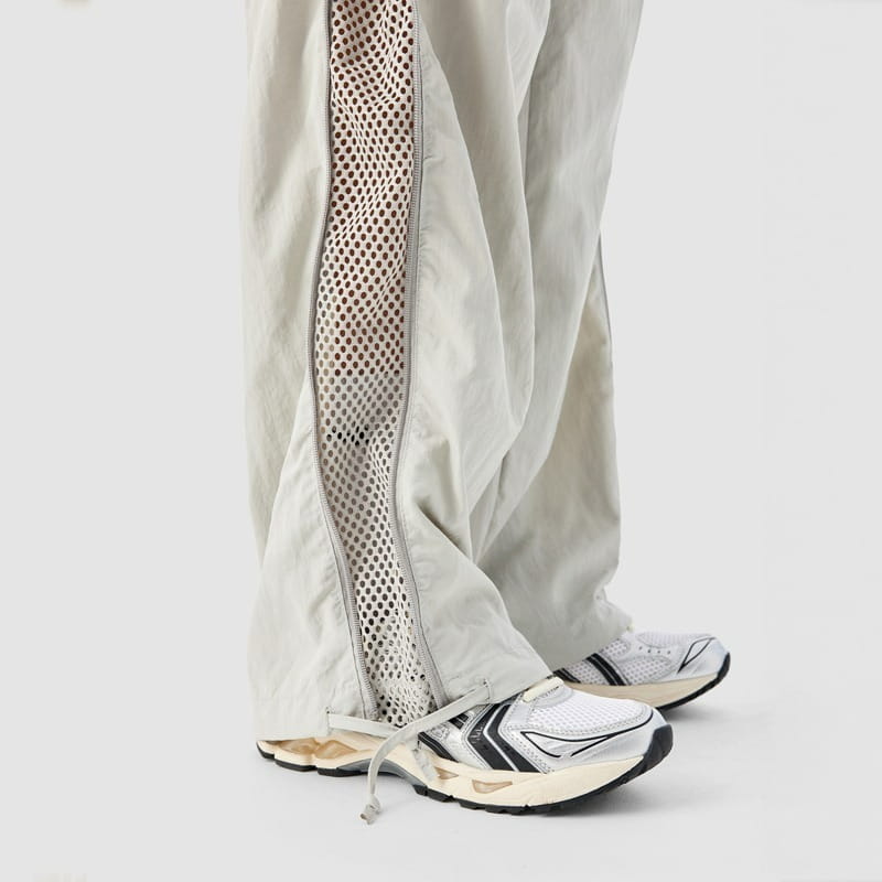 Pantalon de randonnée cargo gris clair avec un panneau latéral en mesh et un détail de fermeture éclair pour l’aération et l’aspect utilitaire.