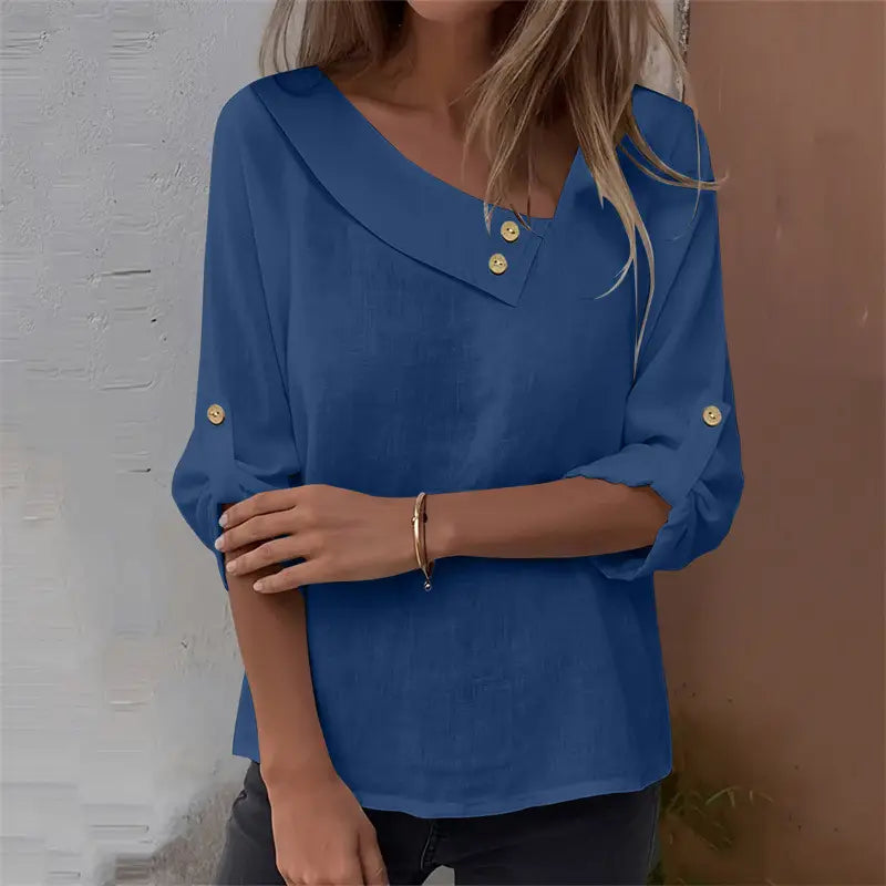 A blue lightweight asymmetric button blouse with a v-neckline and three-quarter sleeves accented by gold buttons at the collar and cuffs.