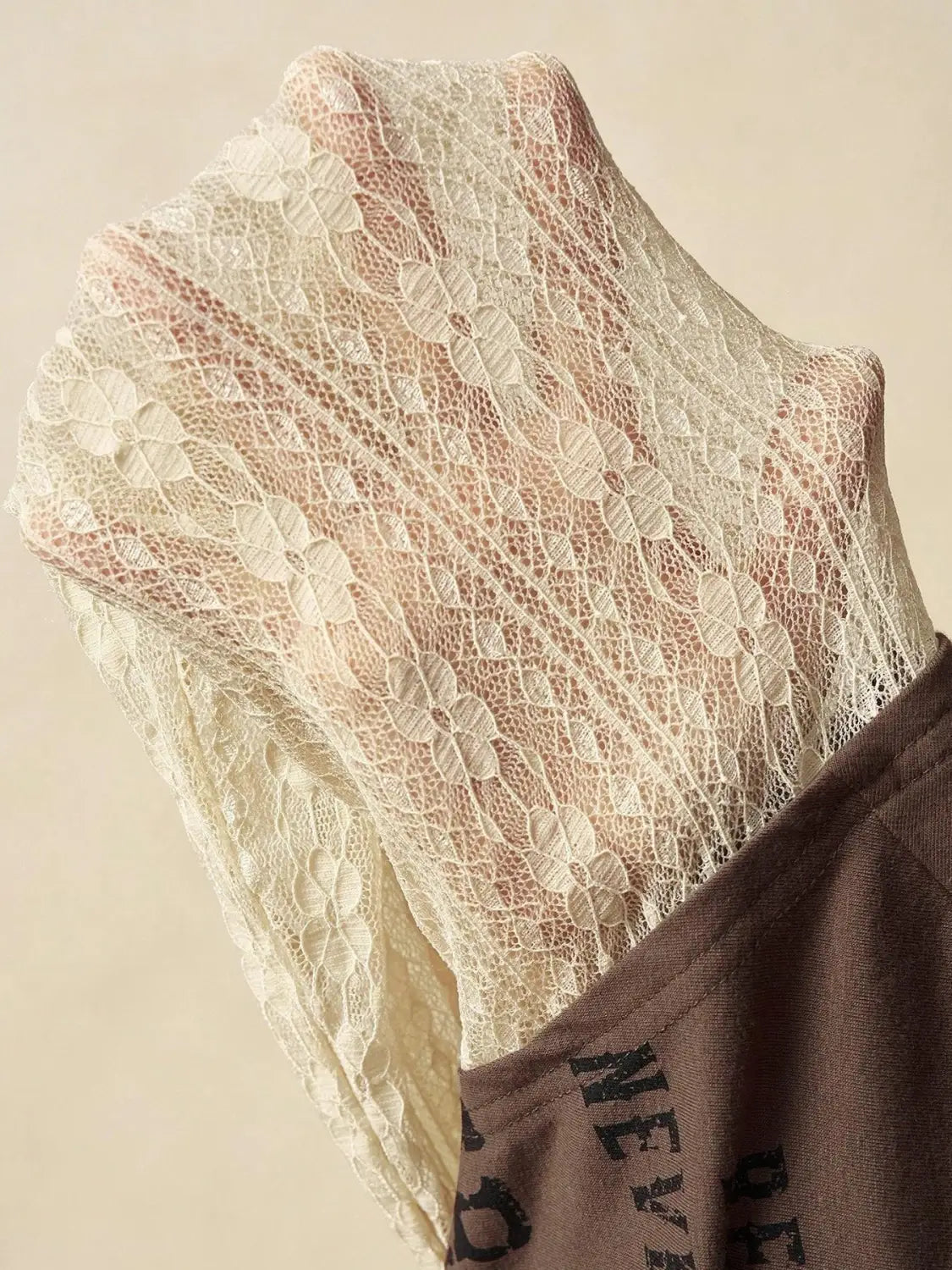 A delicate cream-colored lace layer off shoulder knitted top featuring a floral pattern with an intricate mesh design and soft flowing texture.