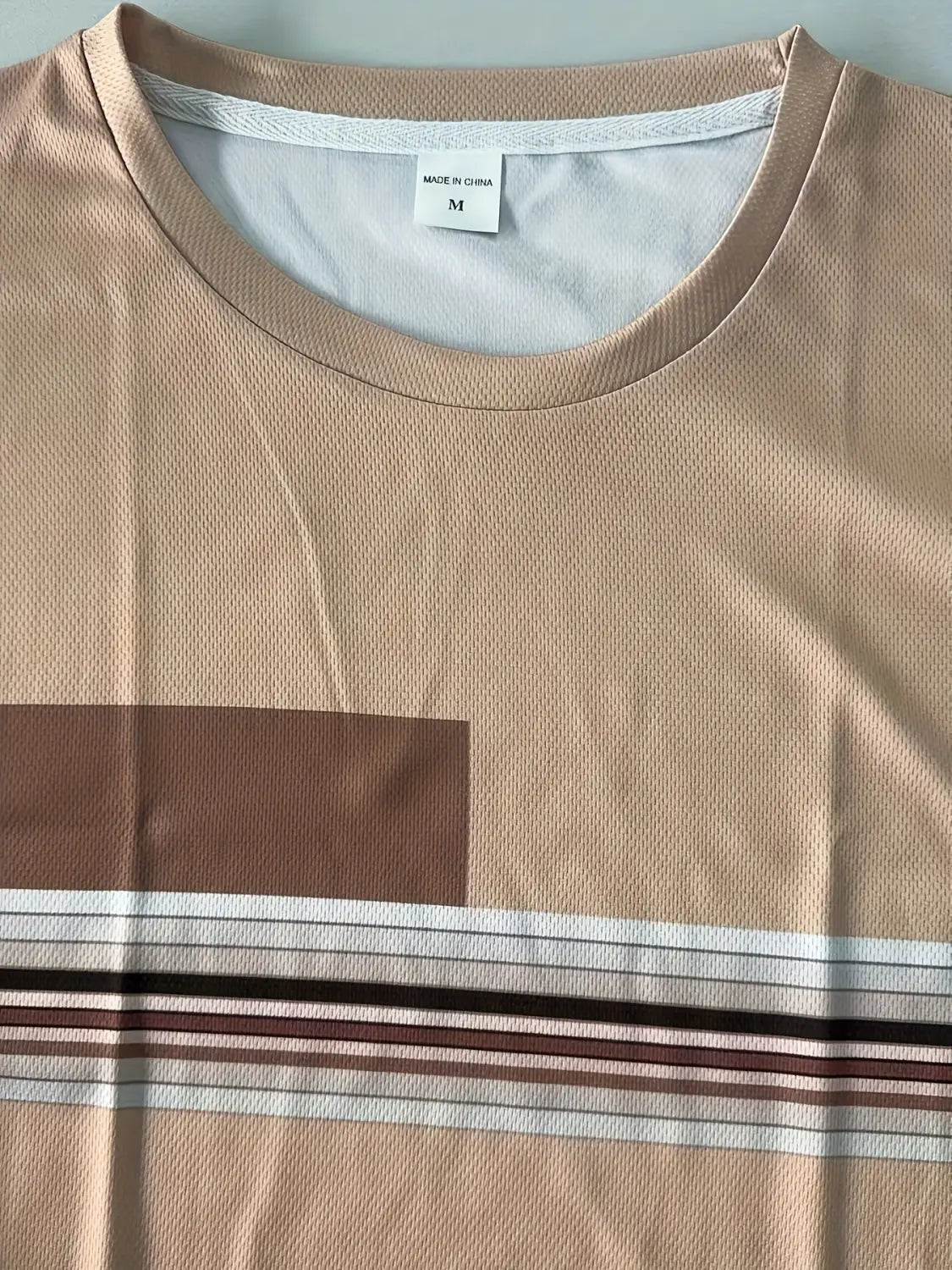 Beige men striped athletic short-sleeved t-shirt with a brown rectangular patch and horizontal stripes in white dark brown and beige suitable for athletic use.