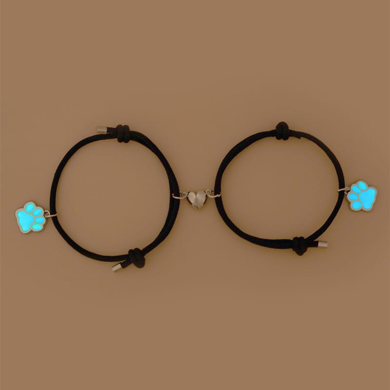 black corded luminous magnetic heart paw print couple bracelets featuring glowing blue paw print charms and a silver heart connector.