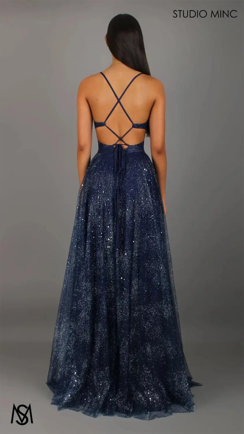 a navy blue sequined shimmering v neck high slit maxi evening gown shown from the back with a crisscross strap design