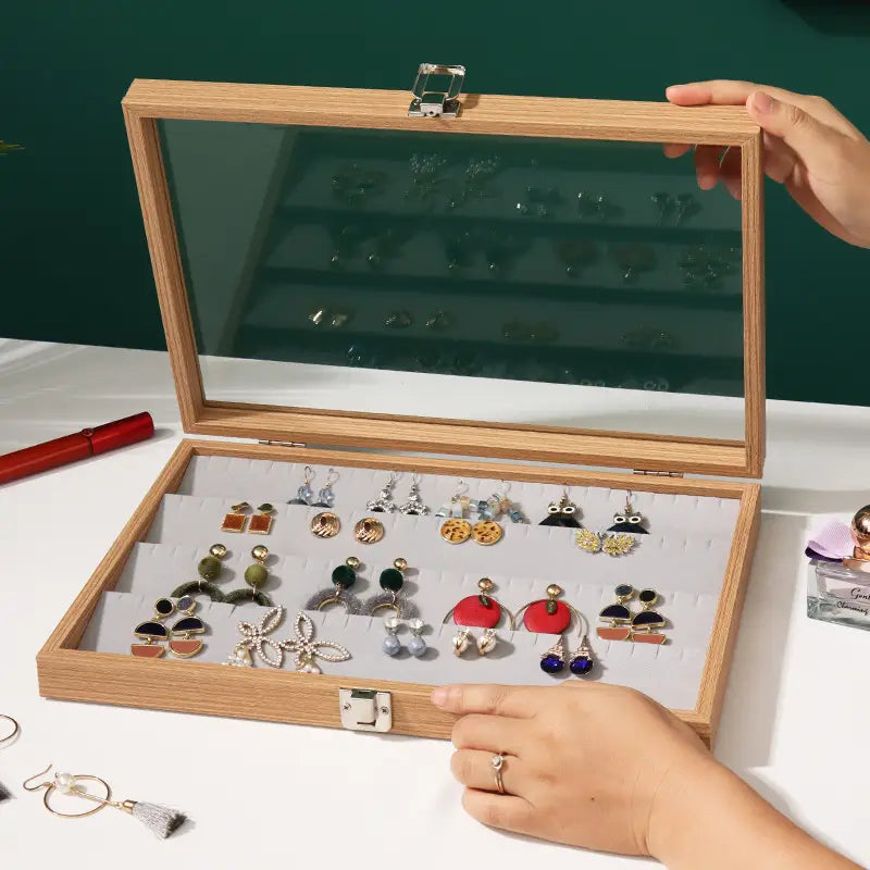 Light wood-finish rectangular rosewood jewelry display box with glass lid and silver-toned latches for earring organization.