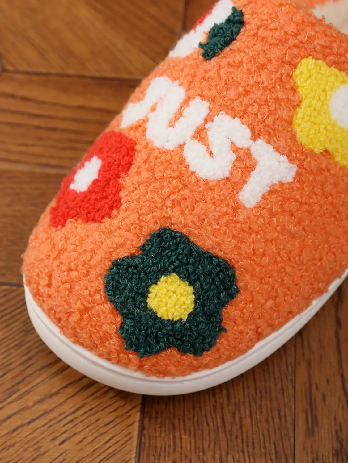 Orange fuzzy plush floral cotton slipper with soft TPR sole featuring embroidered white red yellow and green floral design and just lettering.
