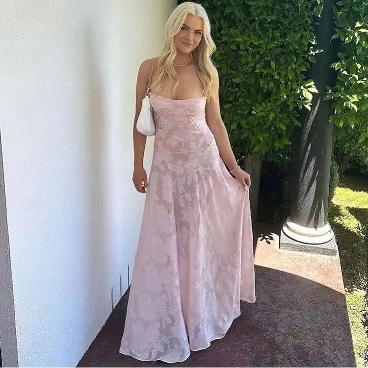Une robe maxi en dentelle à encolure cœur sans bretelles, rose pâle, fluide, avec un motif floral subtil, conçue comme une robe de soirée maxi sans dos en dentelle florale.