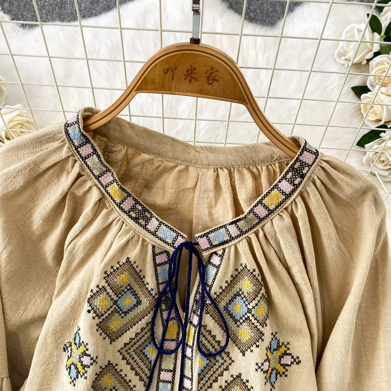 Beige embroidered lantern sleeve tie neck blouse with colorful geometric patterns and a navy blue tie at the neckline.