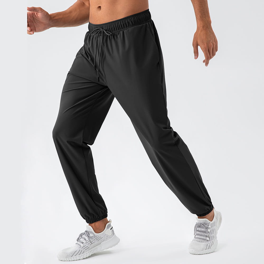Men’s quick dry nylon loose fit athletic track pants in black featuring an elastic waistband with drawstring and tapered legs ending in ribbed cuffs.