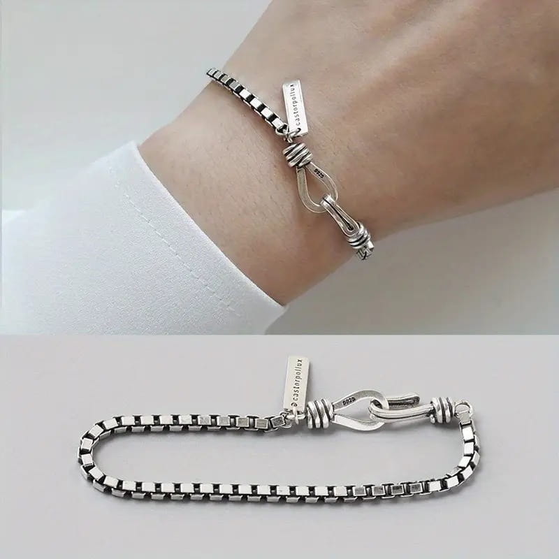Vintage silver box chain cross bracelet with a distinctive knotted clasp and engraved tag featuring a sleek modern silver-toned design.