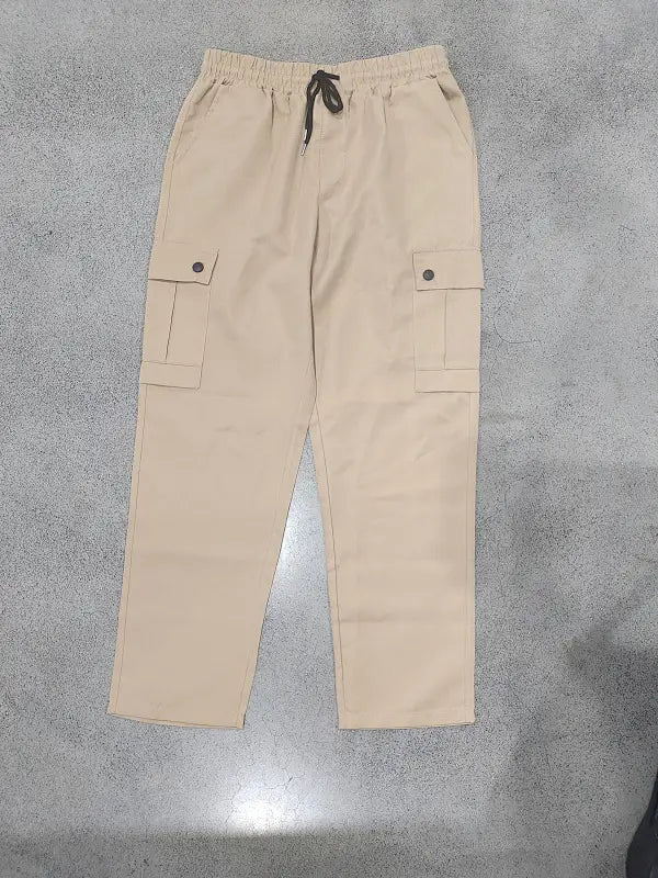 Mens straight leg cargo work pants in beige with an elastic waistband, black drawstring, and two large side flap pockets secured by dark buttons.
