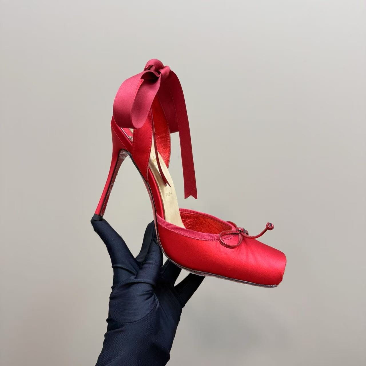 A vibrant red satin high-heeled ballet flat with a leather sole featuring a bow detail on the ankle strap and a small decorative knot at the toe.
