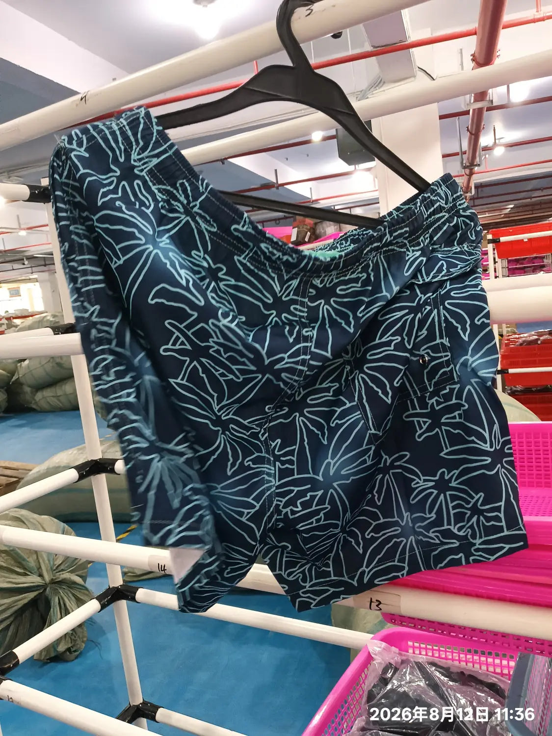 dark blue printed men beach shorts with light blue leaf patterns hanging on a black hanger designed for summer swim trunks.