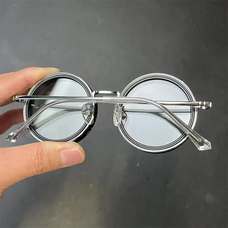 Lunettes de soleil rondes unisexes résistantes aux UV, à monture argent métallique, verres miroir et extrémités de branches claires au rendu cristallin.