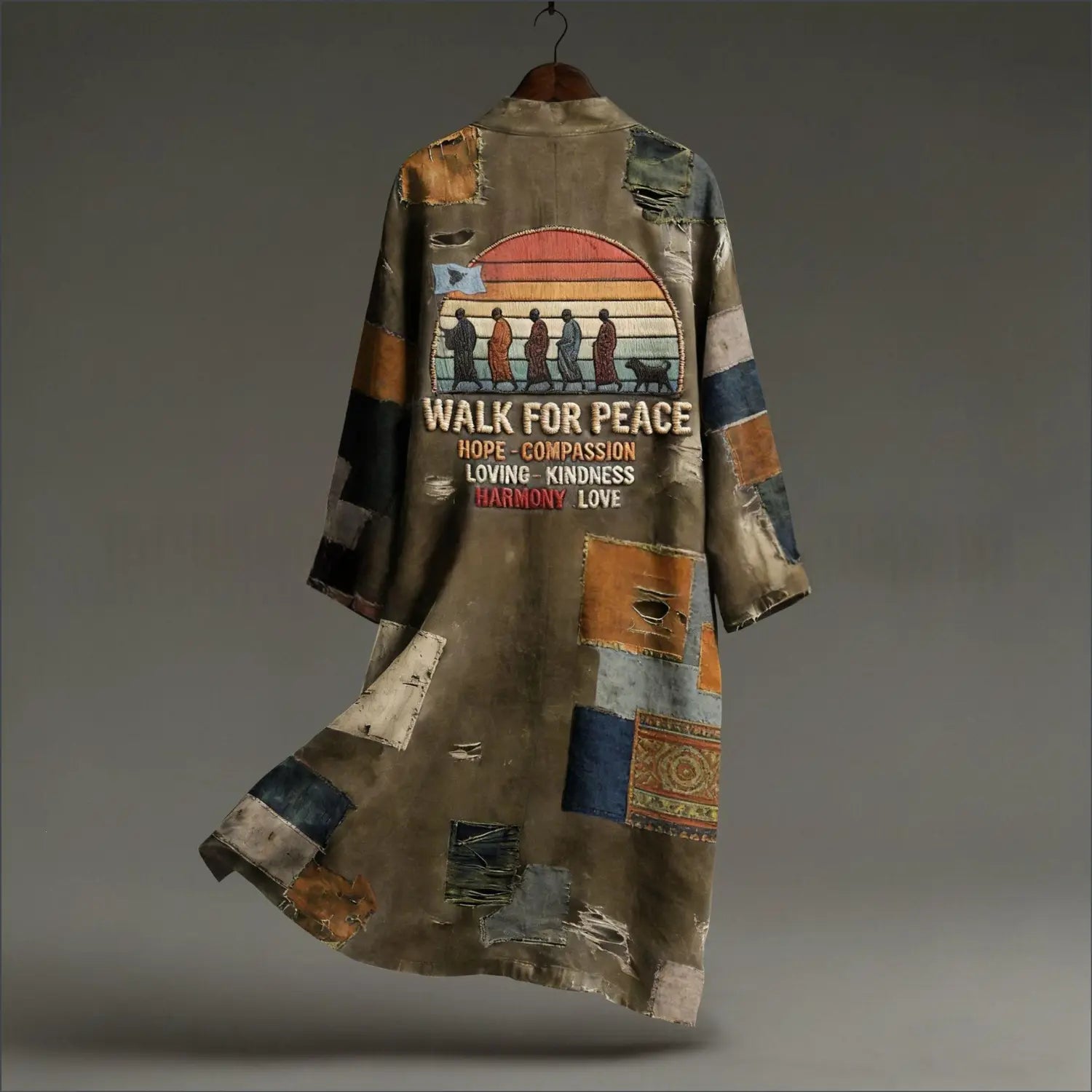 Ein verwitterter Patchwork-Langmantel im gedämpften Erdtönen mit einer Vintage-Sonnenuntergangsgrafik und dem Text „Walk for peace“, der an einem hölzernen Kleiderbügel hängt und von vorne sichtbar ist.