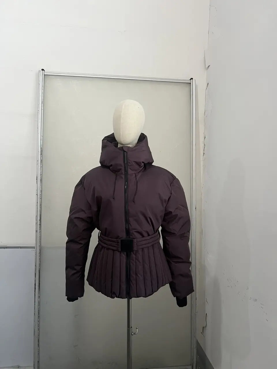 A dark purple women’s belted hooded puffer coat featuring a pleated skirt-like hem and insulated material for cold weather.