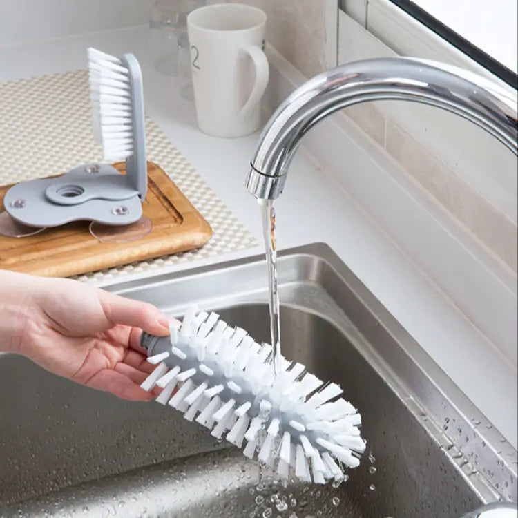 white bristle dish brush with gray handle being rinsed under running water as part of a glass cleaning brush with suction cup sink scrubber set