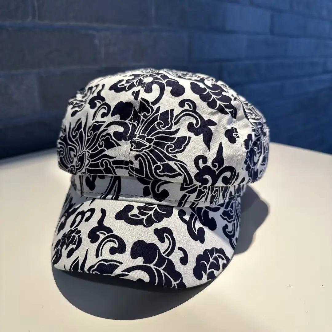 A white fabric floral newsboy cap for women featuring bold black floral and scrollwork patterns.