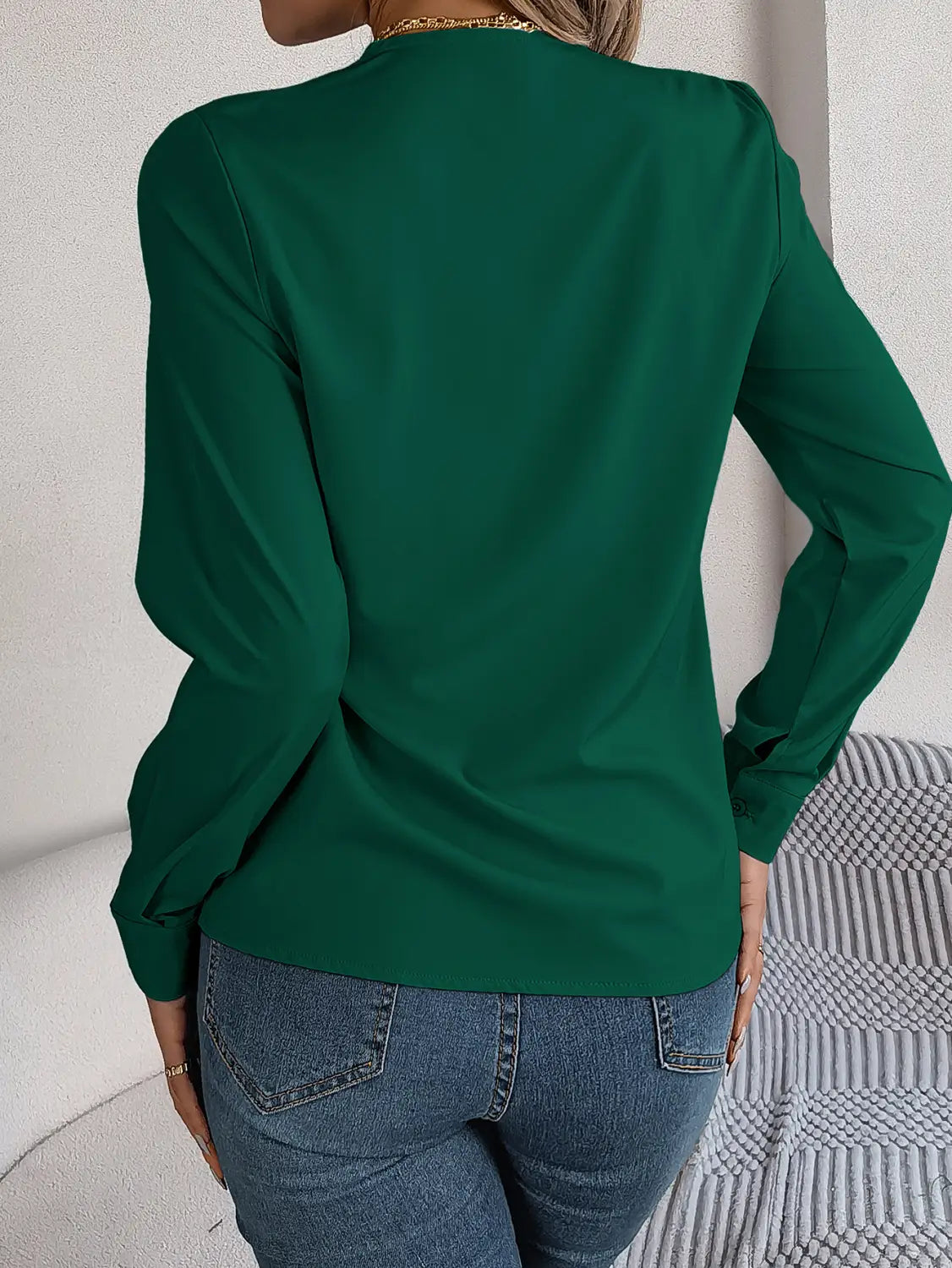 Emerald green long-sleeved blouse with soft flowing fabric and subtle shoulder detailing shown alongside white satin v neck wrap blouse with black trim.