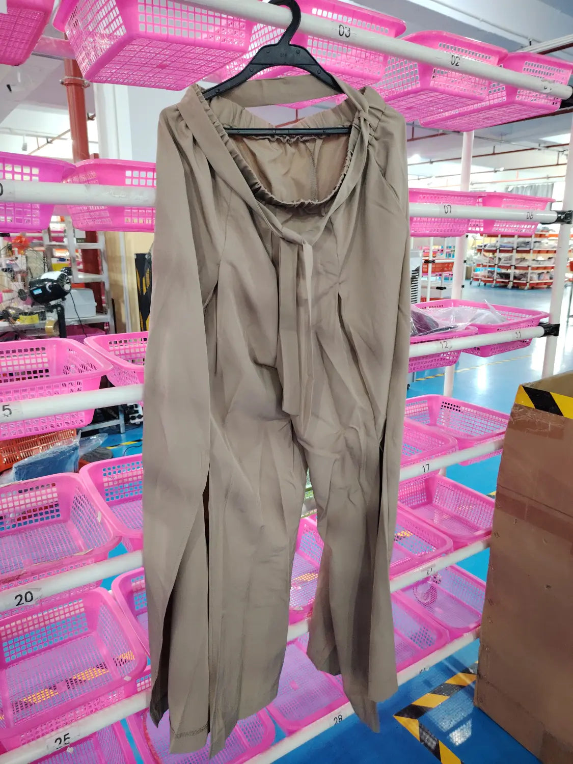 Pantalon ample à taille haute beige avec manches longues, capuche et taille à cordon, suspendu sur un cintre noir.