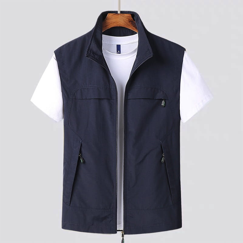 Chaleco utilitario impermeable sin mangas de color azul marino oscuro, con cuello alto, cierre frontal con cremallera y múltiples bolsillos con cremallera.